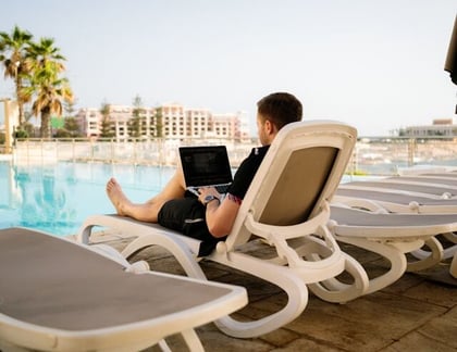man on a lounger by a pool on a laptop - image by humphrey-m - unsplash